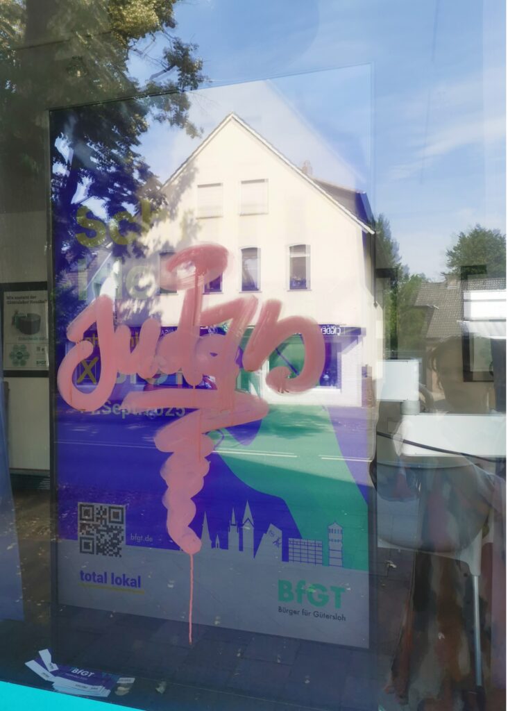 Eine gläserne Werbetafel mit rosa Graffiti und der Aufschrift "Julzo", in deren Glas sich ein Gebäude und Bäume spiegeln.