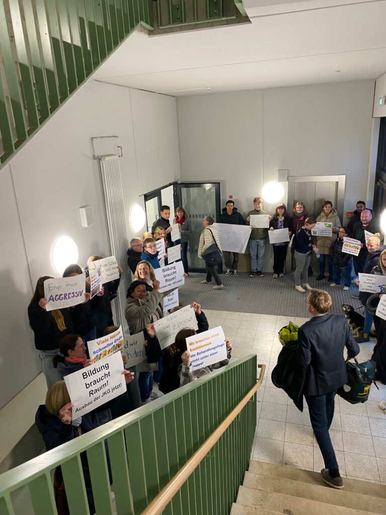 Eine Gruppe von Menschen steht in einem Treppenhaus und hält Protestschilder hoch.